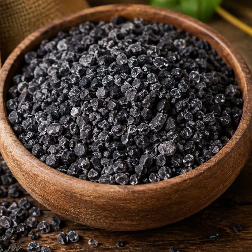 Coarse black salt granules heaped in a wooden bowl.