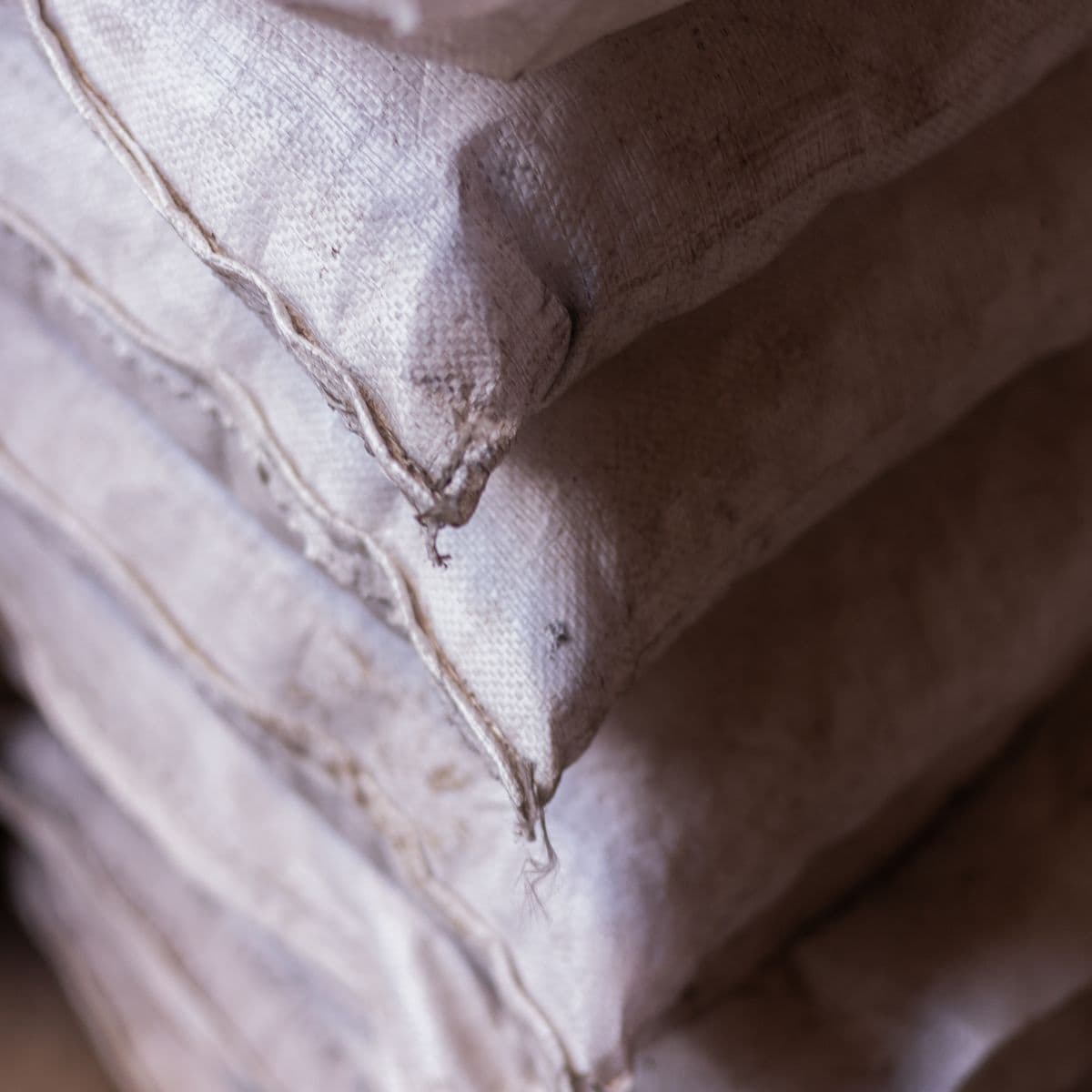 Plain white woven polypropylene sacks stacked in a warehouse, close up.