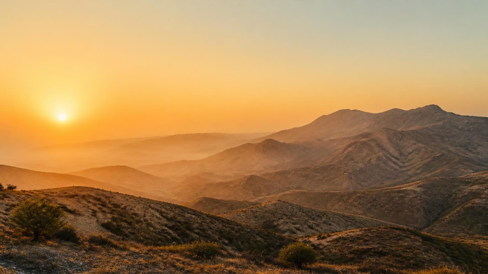 Sunrise over arid, layered foothills, ridgelines receding into haze.