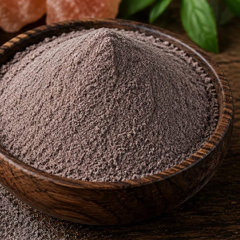 Black salt milled to a pink-grey powder, mounded in a wooden bowl.